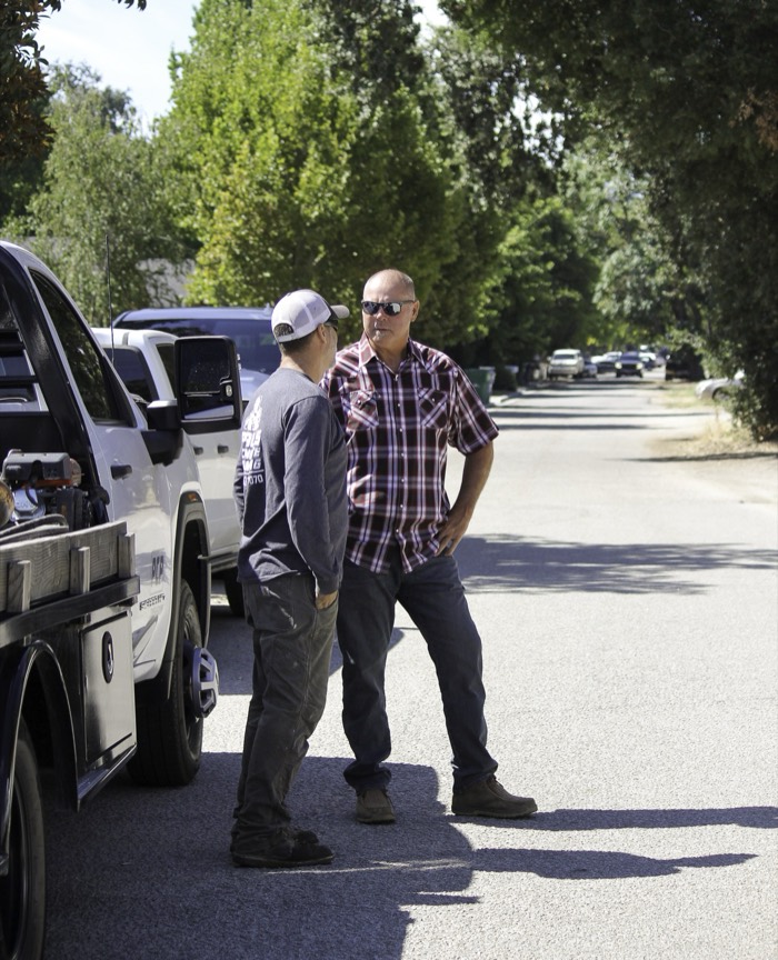 Mike Avila talking with a worker beside a white service truck on a tree-lined street