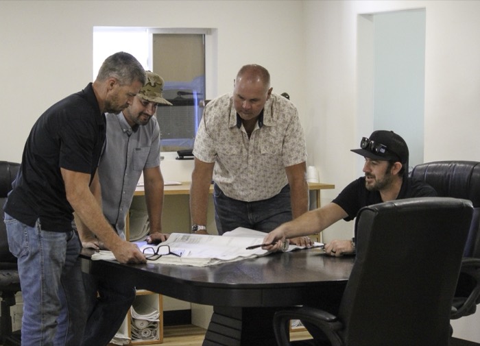 Mike Avila and three colleagues standing around a conference table reviewing plans and paperwork