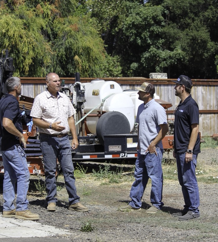 Mike Avila talking with three workers in a yard beside a trailer-mounted water tank
