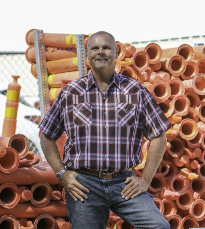 Mike Avila standing in front of stacked orange traffic barrels at an equipment yard