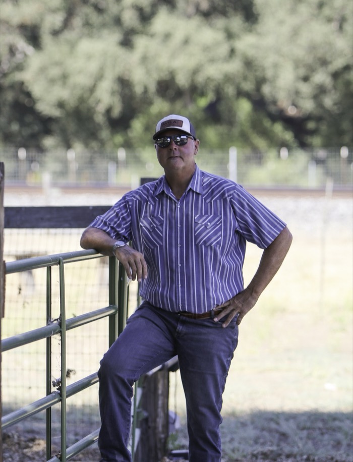 Mike Avila leaning against a metal gate at a rural property