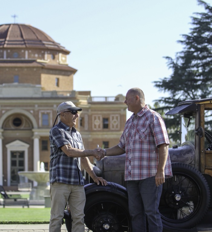 Mike Avila shaking hands with a man beside a vintage car in front of the Atascadero City Hall rotunda